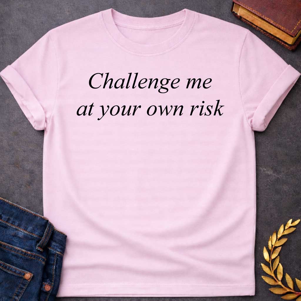 Light Pink T-shirt graphic in black featuring large elegant italic serif text reading "Challenge me at your own risk" — a bold warning referencing Athena, the Greek Goddess of Wisdom and War Strategy