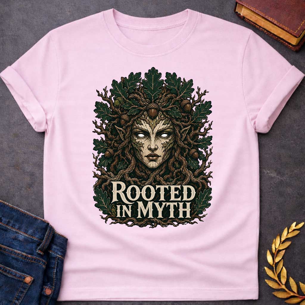 Light Pink T-shirt with a detailed cottagecore-style graphic featuring a powerful oak tree dryad or nature spirit. Her intense face, with glowing white eyes, is framed by gnarled, twisting branches and a thick canopy of dark green oak leaves and brown acorns. Interwoven with the roots at the bottom, the bold, stylized cream text reads "ROOTED IN MYTH," creating a striking, mythical, and nature-inspired apparel design