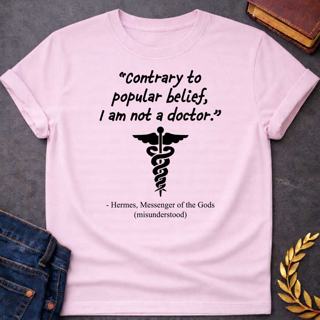 Light Pink T-shirt graphic in black text featuring a handwritten-style quote reading "Contrary to popular belief, I am not a doctor." above a black caduceus symbol, with the humorous attribution below in serif text reading "- Hermes, Messenger of the Gods (misunderstood)," playing on the common confusion between Hermes' caduceus and the medical symbol