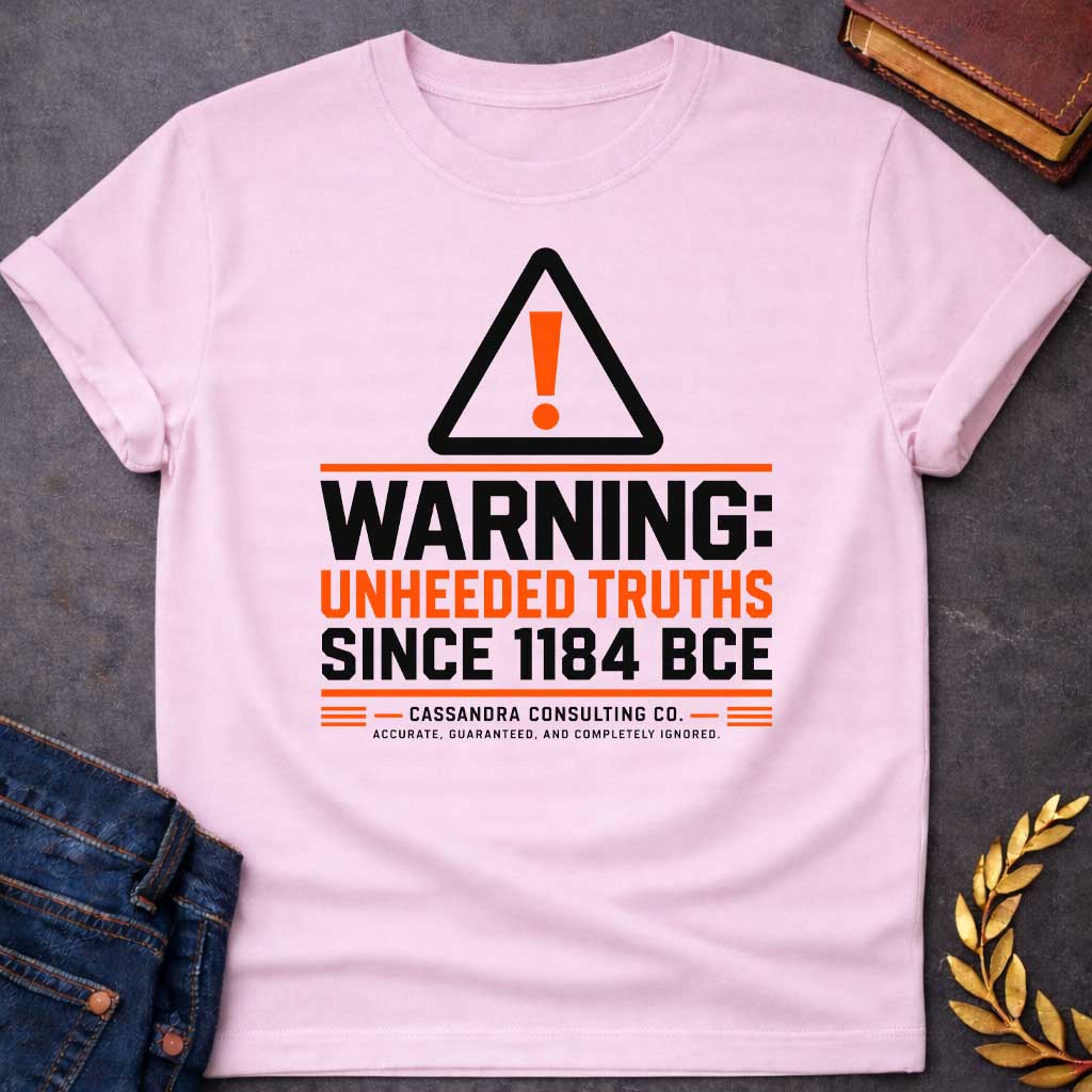 Light Pink T-shirt with a corporate-style satirical design mimicking an industrial hazard sign. At the top is a triangular warning icon with an orange exclamation point. Bold block text reads "WARNING: UNHEEDED TRUTHS SINCE 1184 BCE" in alternating black and orange. Below, it features a faux company name: "CASSANDRA CONSULTING CO." followed by the tagline, "ACCURATE, GUARANTEED, AND COMPLETELY IGNORED."