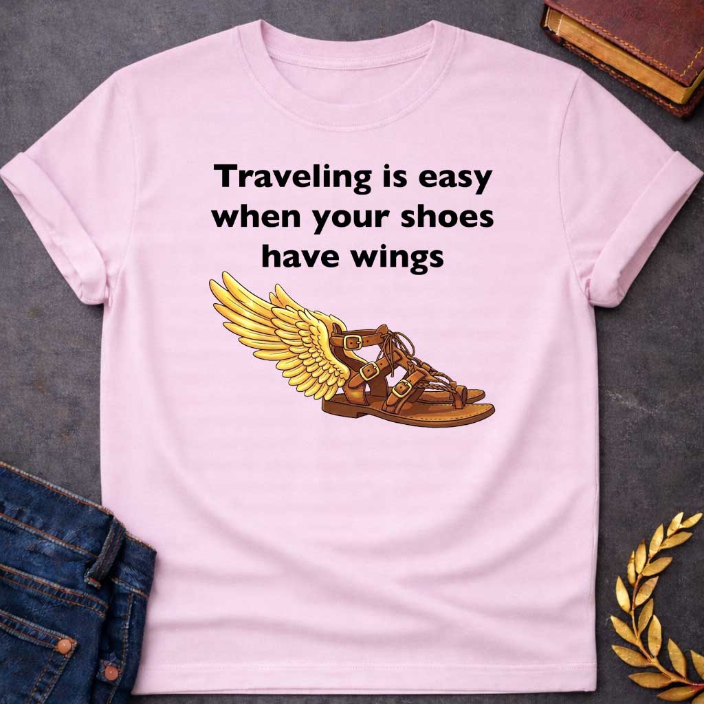 Light Pink T-shirt graphic featuring bold black text reading "Traveling is easy when your shoes have wings" above a detailed illustration of Hermes' winged sandal, depicted as a brown leather gladiator sandal with gold buckles and braided lacing, with a large golden wing extending from the ankle — a humorous reference to the talaria, the iconic flying sandals of Hermes, the Greek Messenger God