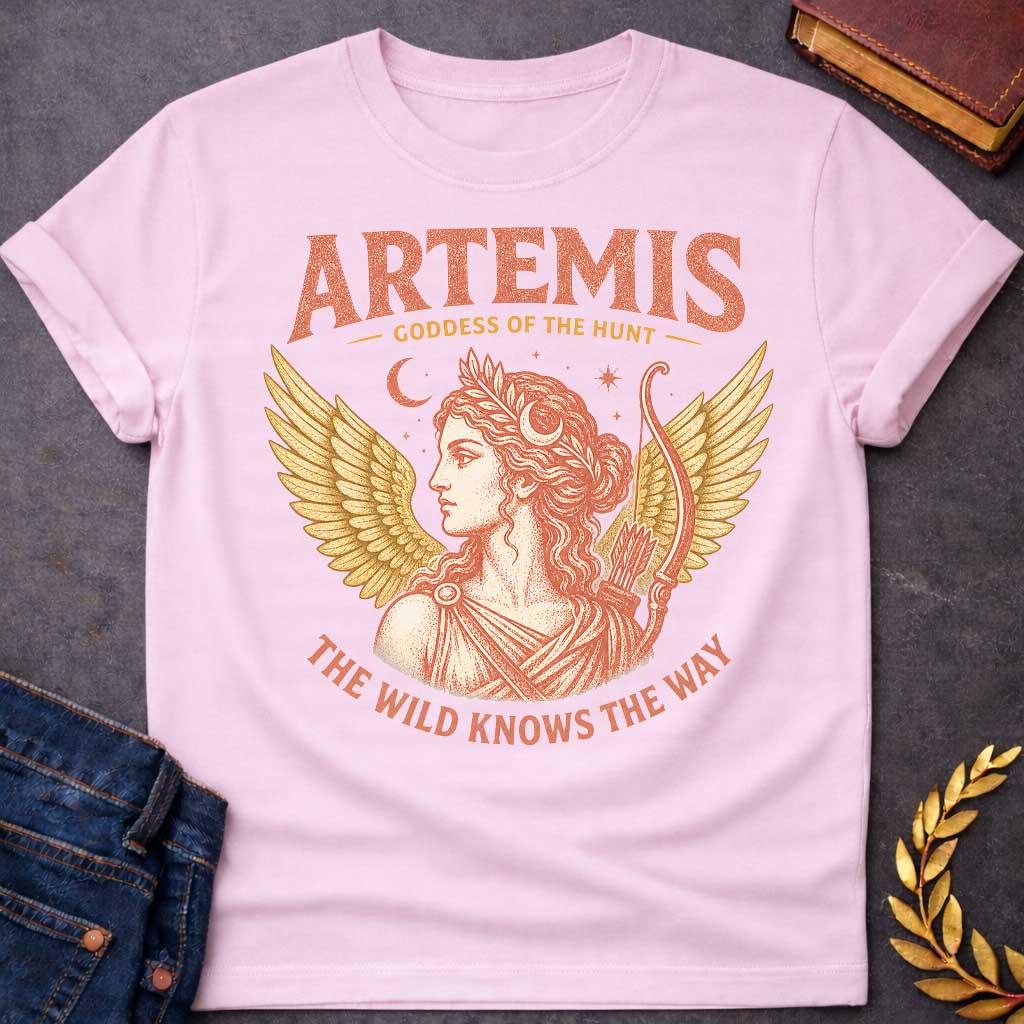 Light Pink t-shirt with a Vintage Greek mythology design featuring Artemis, goddess of the hunt, with a crescent moon, stars, bow and arrows, and golden wings. Warm coral and gold engraving-style artwork frames her classical portrait. Bold text reads "Artemis – Goddess of the Hunt" and "The Wild Knows the Way," celebrating the Olympian goddess of nature and the hunt.