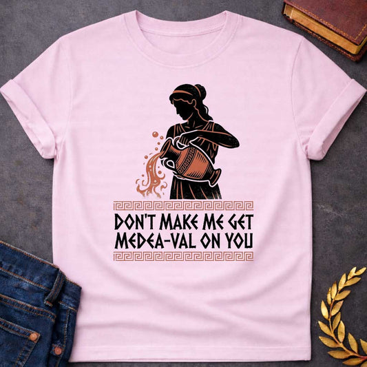 Light Pink T-shirt with A Silhouetted figure of Medea, legendary Greek sorceress, rendered in black and rust-red. She wears classical robes and headband while holding an ornate cauldron with magical flames and sparks bursting forth. Greek key pattern borders frame the design. Text reads 'Don't Make Me Get Medea-Val On You' - wordplay combining her name with modern slang. Celebrates Medea's fearsome magical and destructive powers with contemporary humor.