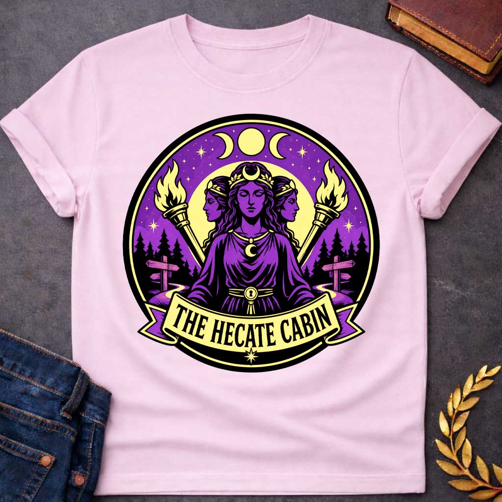 Light Pink t-shirt with a Hecate Greek mythology design featuring the triple goddess with three faces, crescent moon symbols, glowing torches, stars, and a mystical purple night sky. Forest silhouettes and crossroads signs represent Hecate’s connection to magic and crossroads, framed in a circular camp-style emblem with the text “The Hecate Cabin.”