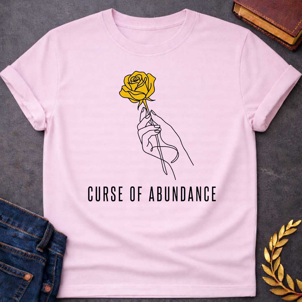 Light Pink t-shirt with A Minimalist Greek mythology design featuring a continuous line-art hand delicately holding a golden rose, symbolizing King Midas' legendary golden touch. Below the illustration, the phrase "Curse of Abundance" appears in clean, modern typography. A simple black-and-gold aesthetic creates an elegant, understated design inspired by the tragic Midas myth.