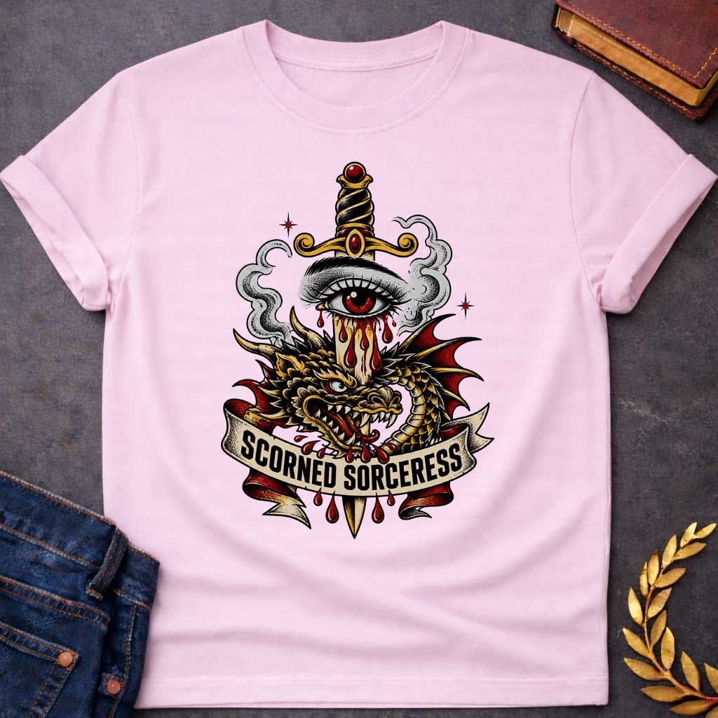 Light Pink T-shirt featuring traditional tattoo-style artwork: a gold-hilted dagger with black-and-gold wrapped handle and ruby pommel pierces through a weeping red-irised eye, blood streaming down the blade. A gold and red dragon coils around the dagger, fangs bared, with grey smoke curling behind. A cream ribbon banner below reads "Scorned Sorceress" in bold black lettering, dripping blood, on a white background.