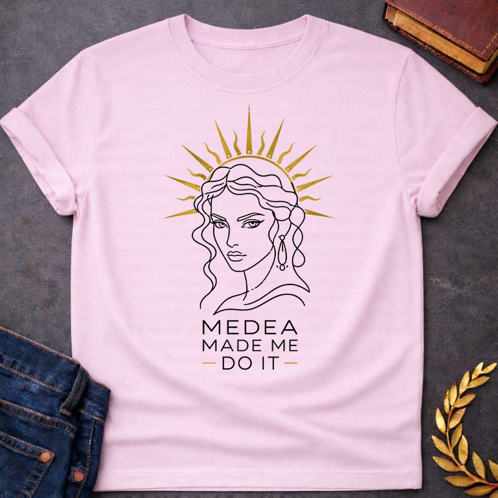 Light PInk T-shirt with a Minimalist line art portrait of Medea with wavy hair and drop earrings, framed by a golden radiating sun halo. Black and white design with gold accents. Text reads 'Medea Made Me Do It.' Humorous reference to blaming the legendary Greek sorceress for chaotic or destructive actions. Celebrates Medea's infamous power and magical influence with tongue-in-cheek blame attribution.