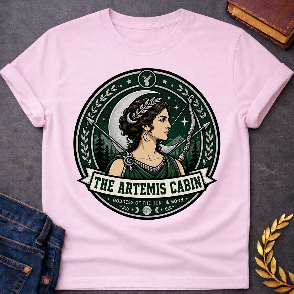 Light Pink t-shirt with a Artemis Greek mythology cabin design featuring the goddess of the hunt and moon with a crescent moon, bow and arrows, forest mountains, stars, laurel branches, and deer symbol. Dark green, silver, cream, and black circular camp-style emblem includes the text “The Artemis Cabin” and “Goddess of the Hunt & Moon.”