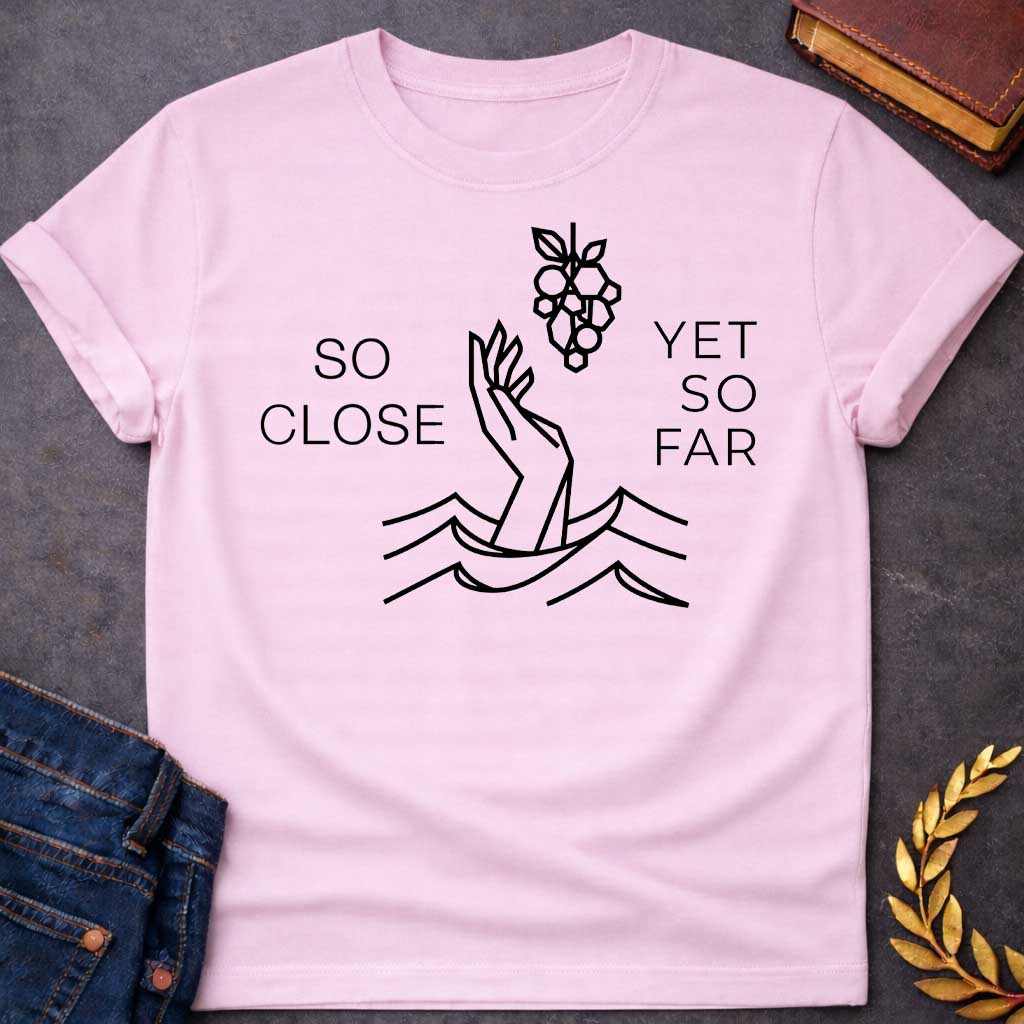 Light Pink t-shirt with A minimalist, geometric line-art design. Rendered in crisp black lines, a stylized hand reaches out from geometric water waves toward a cluster of grapes hanging above it. Simple, thin sans-serif text flanks the central illustration, with "SO CLOSE" stacked on the left and "YET SO FAR" stacked on the right.