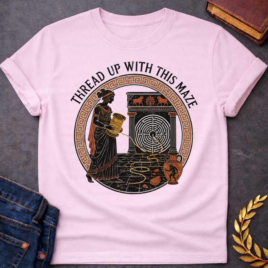 Light Pink T-shirt with A distressed, ancient Greek pottery-style t-shirt graphic. Inside a circular terracotta Greek key frame, a black figure of Ariadne holds a large spool, unwinding a golden thread that leads into a circular maze on a stone structure. An amphora vase with a Minotaur stands nearby. Arched above the scene, black text reads "THREAD UP WITH THIS MAZE" in a rustic serif font.
