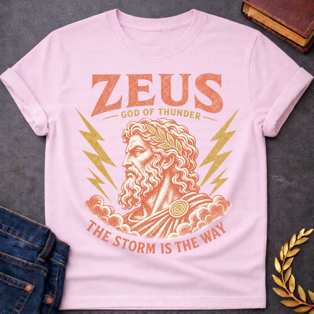 Light Pink t-shirt with a Vintage Zeus Greek mythology design featuring the bearded god of thunder wearing a golden laurel crown, surrounded by lightning bolts and storm clouds. Distressed terracotta and gold artwork includes the text “Zeus,” “God of Thunder,” and “The Storm Is the Way,” 