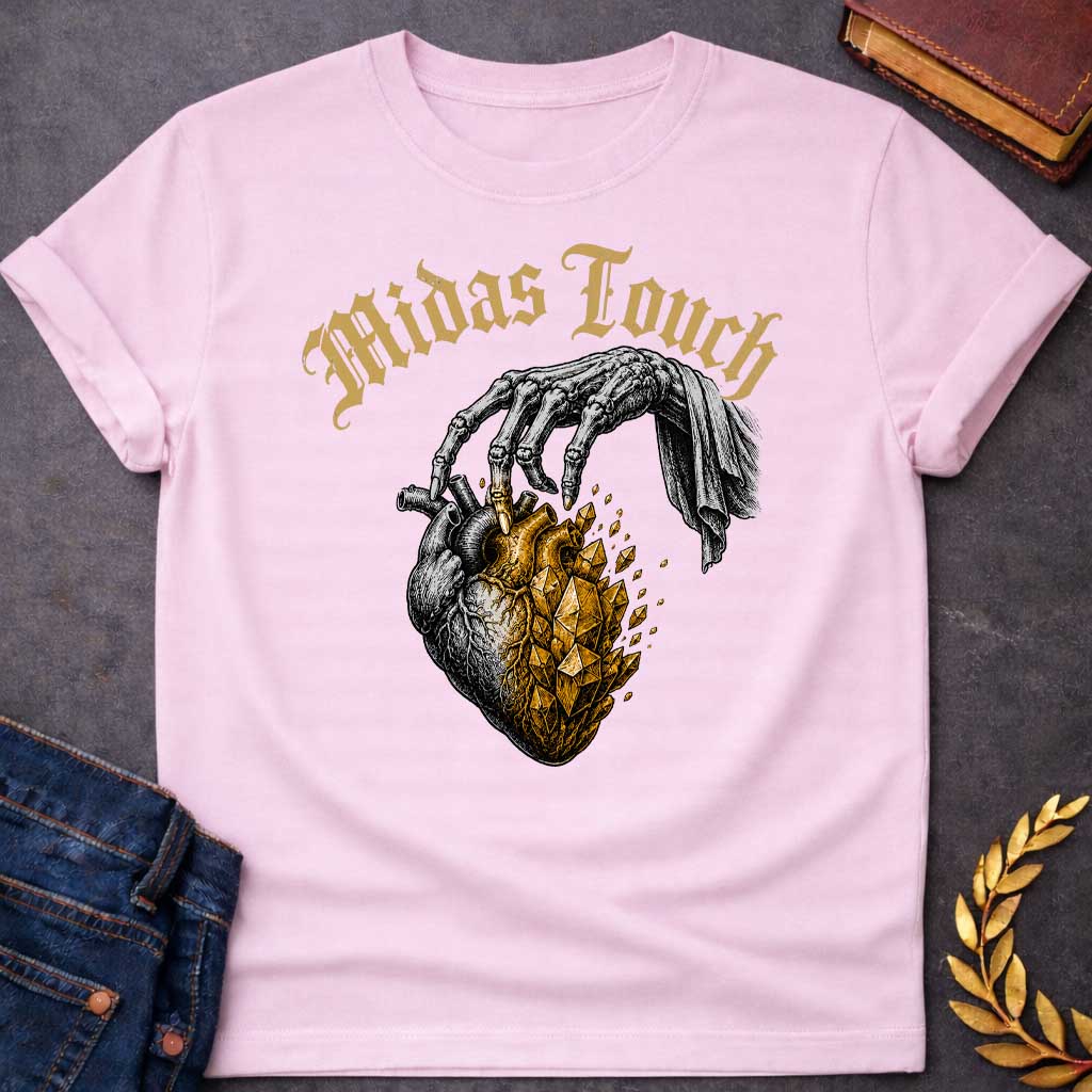Light Pink t-shirt with A Vintage engraving-style Greek mythology design featuring a skeletal hand with the Midas touch transforming half of an anatomical heart into shimmering gold crystals. Above the illustration, gothic lettering reads "Midas Touch." Inspired by the tragic King Midas myth, the design symbolizes how greed and the pursuit of wealth can harden the heart, using bold black and metallic gold artwork.