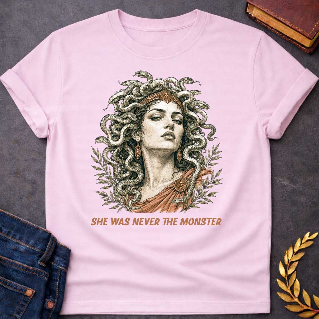 Light Pink t-shirt with A Detailed vintage engraving-style Greek mythology t-shirt design featuring Medusa with an intense expression, a crown, and numerous snakes twisting through her hair. Olive branches frame the portrait, with bronze and terracotta accents adding an ancient classical feel. Bold text below reads "She Was Never the Monster," creating a dramatic reinterpretation of the Medusa myth.
