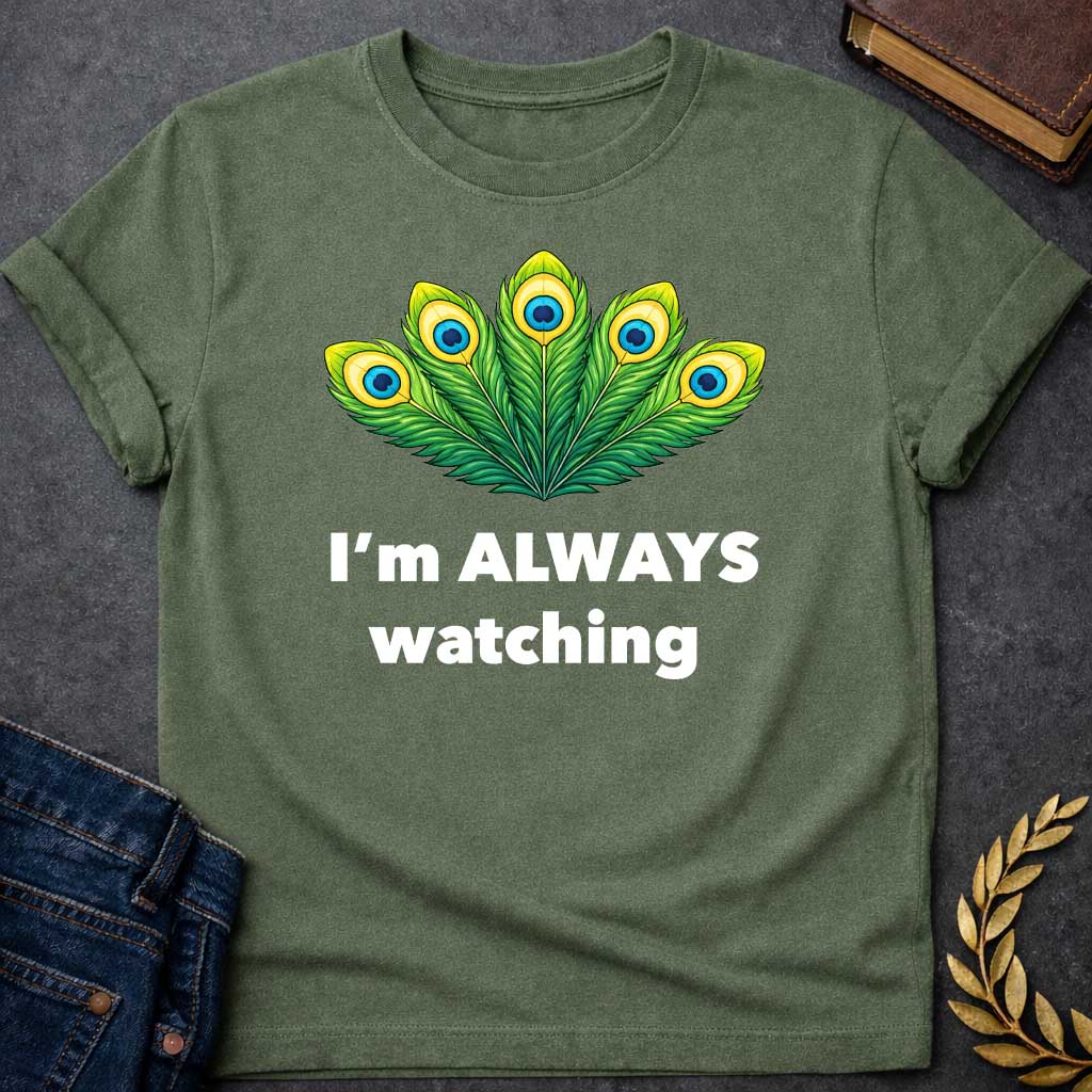 Military Green T-shirt graphic featuring a vibrant illustrated fan of five peacock feathers in rich green, yellow, and blue tones, each with a distinctive eye-spot, above text reading "I'm Always Watching" — a humorous reference to Hera, the Greek Queen of the Gods, whose sacred symbol is the peacock