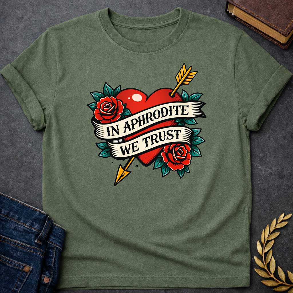 Military Green T-shirt graphic in a classic American traditional tattoo style featuring a bold red heart pierced diagonally by a gold arrow, flanked by two red roses with teal green leaves, with a cream scroll banner wrapped around the heart reading "In Aphrodite We Trust" in black serif text — referencing Aphrodite, the Greek Goddess of Love, and Eros whose golden arrow inspired love