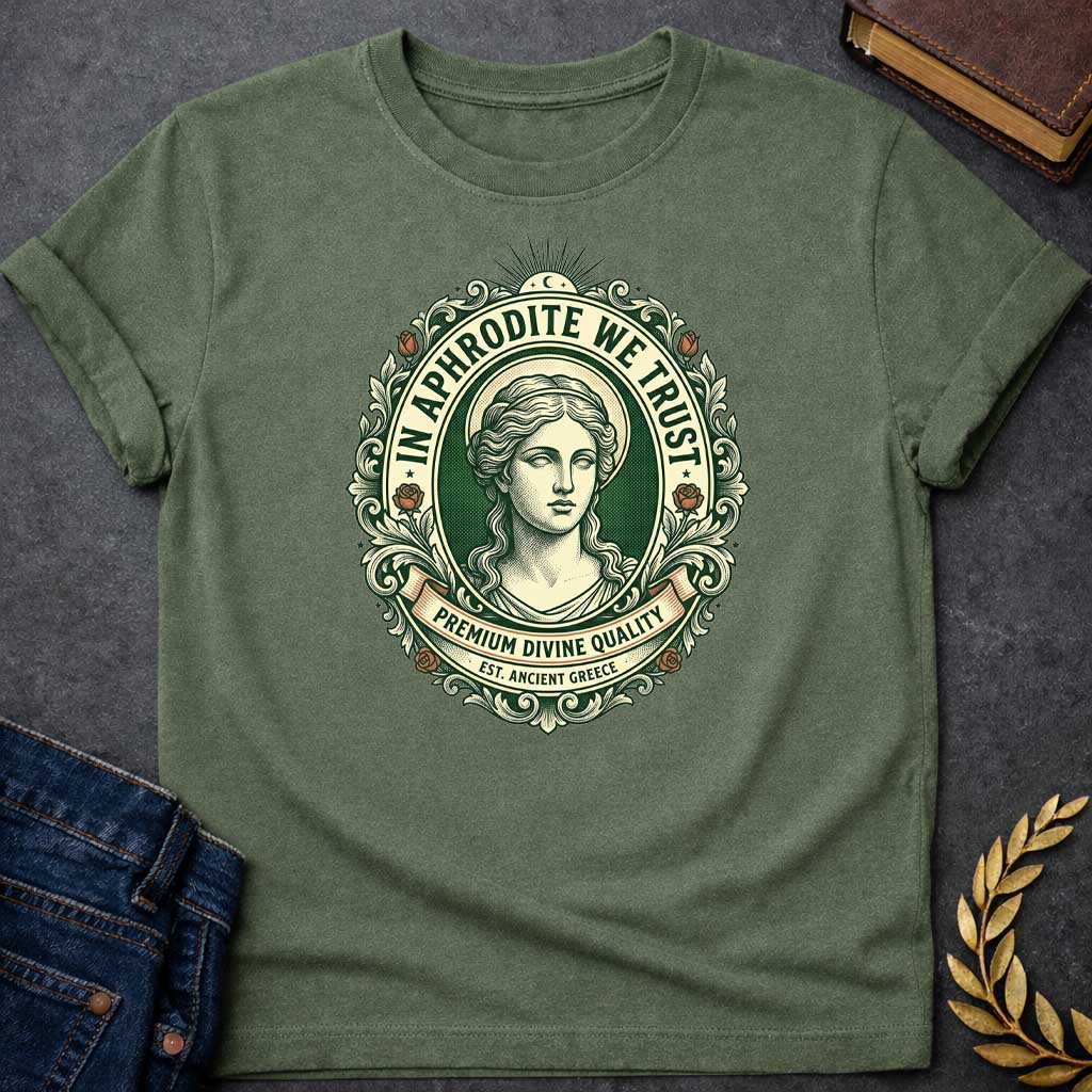 Military Green T-shirt graphic featuring a vintage apothecary label-style oval badge design in forest green, cream, and terracotta. A detailed engraving-style portrait of Aphrodite is centered within the badge, surrounded by ornate scrollwork and flanked by red roses, with a crescent moon and sunburst radiating from the top. Text arched around the inner circle reads "In Aphrodite We Trust," with a scroll banner below reading "Premium Divine Quality" and smaller text underneath reading "Est. Ancient Greece,"