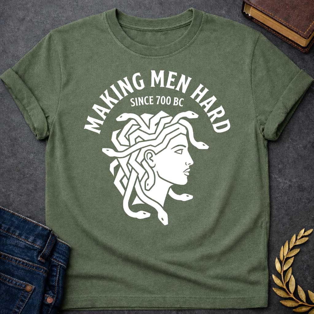 Military Green T-shirt graphic white featuring a bold flat graphic side-profile illustration of Medusa with snake hair, in a minimalist ancient Greek coin or seal style. Bold arched text above reads "Making Men Hard" with smaller text below it reading "Since 700 BC" — a witty double entendre referencing Medusa's mythological power to turn men to stone