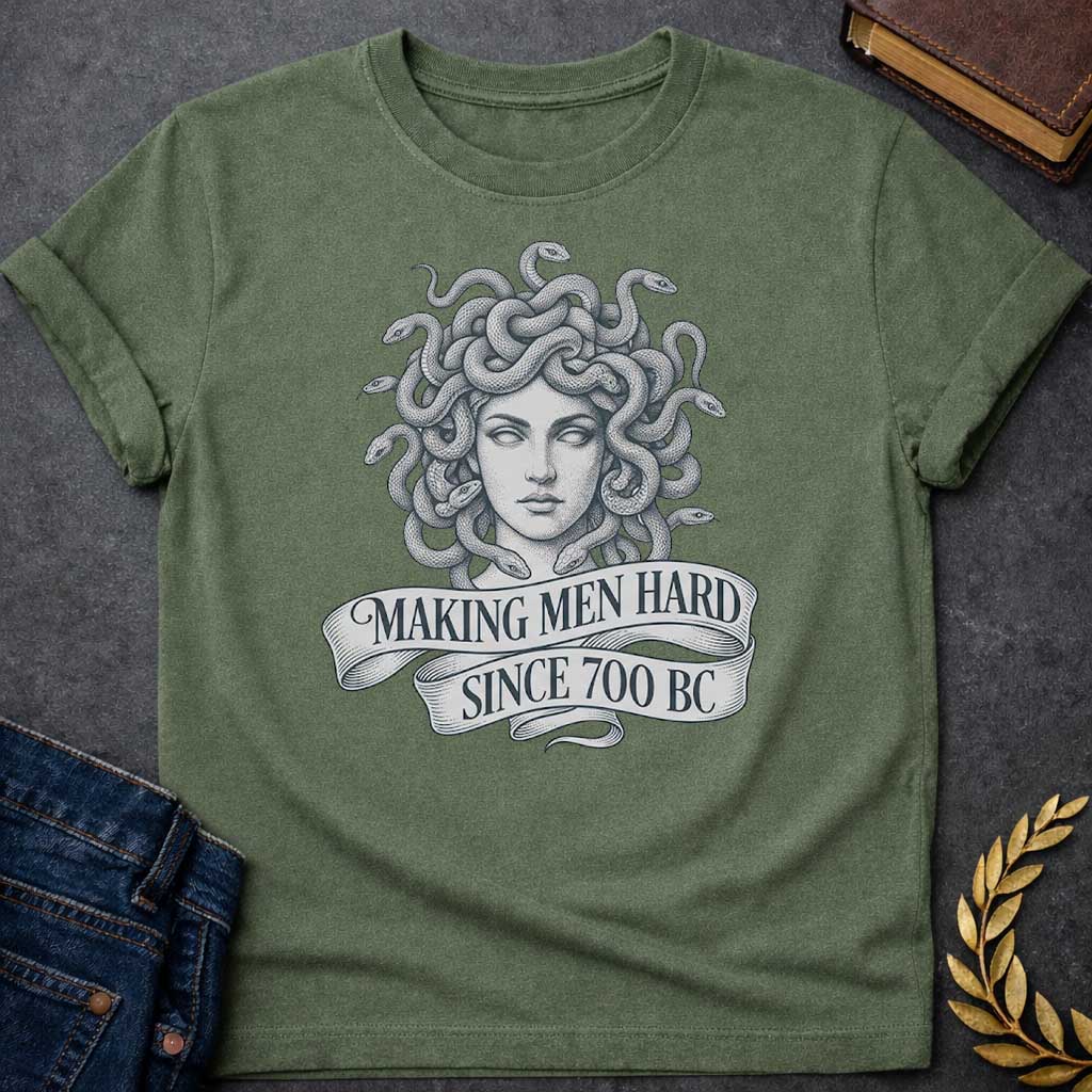 Military Green T-shirt graphic in grey and white featuring a highly detailed fine-line tattoo-style front-facing portrait of Medusa with numerous coiling snakes for hair, rendered in intricate stippling and engraving technique, with a flowing ribbon banner below reading "Making Men Hard Since 700 BC" — a witty double entendre referencing Medusa's mythological power to turn men to stone