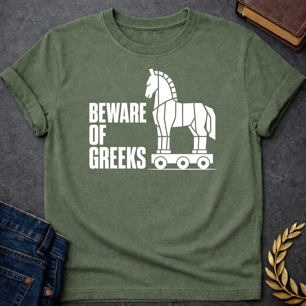 Military Green T-shirt with a graphic in white featuring bold condensed sans-serif text reading "Beware of Greeks" alongside a flat geometric white silhouette illustration of the Trojan Horse mounted on a wheeled platform — a humorous reference to the Greek legend of the Trojan War