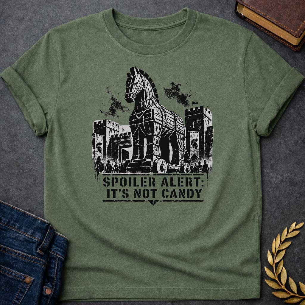 Military Green T-shirt with a graphic in black featuring a gritty detailed ink splatter-style illustration of the Trojan Horse towering over the walls of Troy, flanked by Spartan warriors with shields and spears and castle battlements with birds circling overhead. Bold military stencil text in a distressed banner below reads "Spoiler Alert: It's Not Candy" — a humorous reference to the Greek legend of the Trojan War