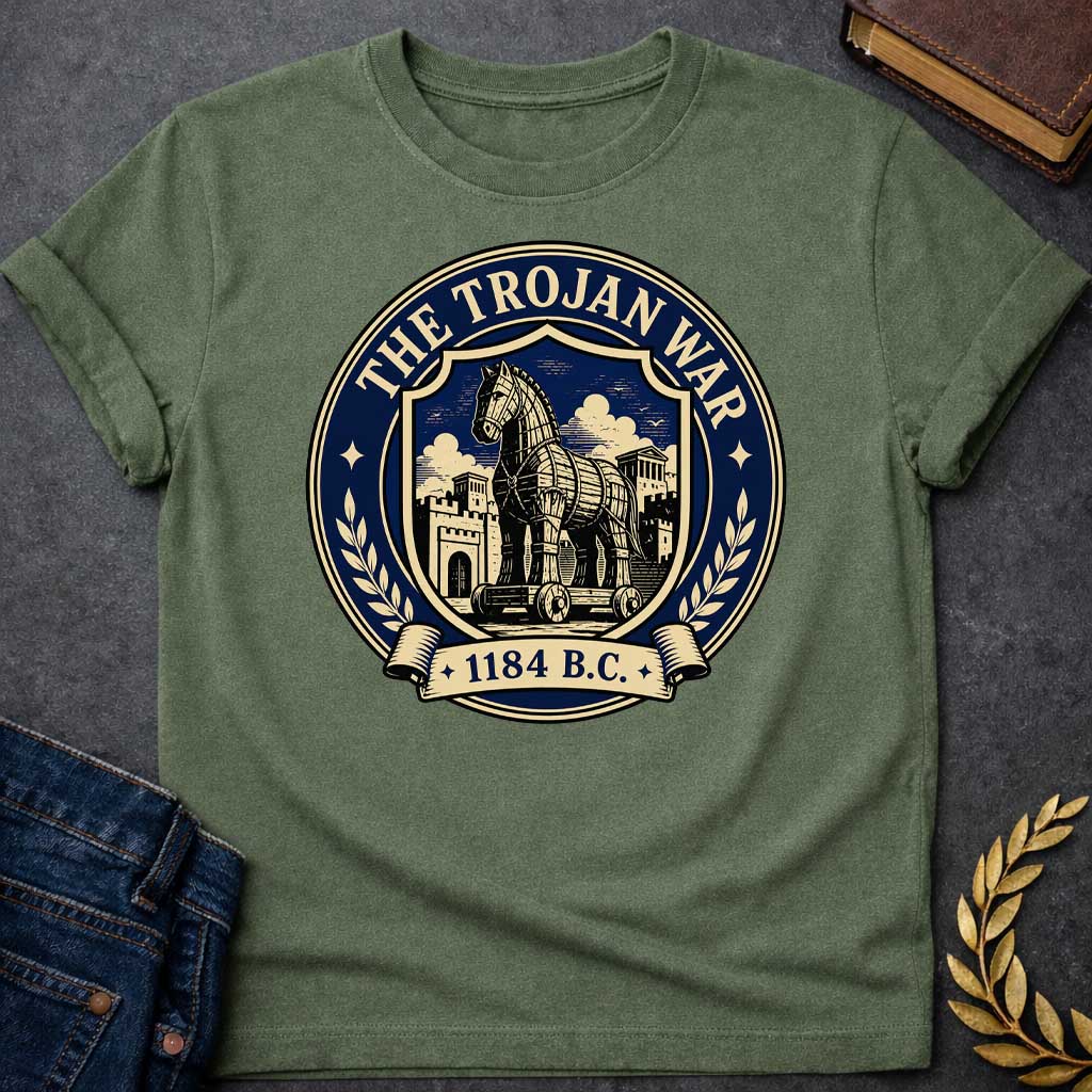 Military Green T-shirt with a graphic featuring a formal vintage seal design in navy and cream. A detailed engraving-style illustration of the Trojan Horse on wheels is centered within a shield, set against the walled city of Troy with Greek temple columns and dramatic clouds. Text arched around the outer circle reads "The Trojan War" with gold diamond stars, flanked by cream laurel branches, and a scroll banner below reads "1184 B.C." — referencing the legendary Trojan War from Greek mythology
