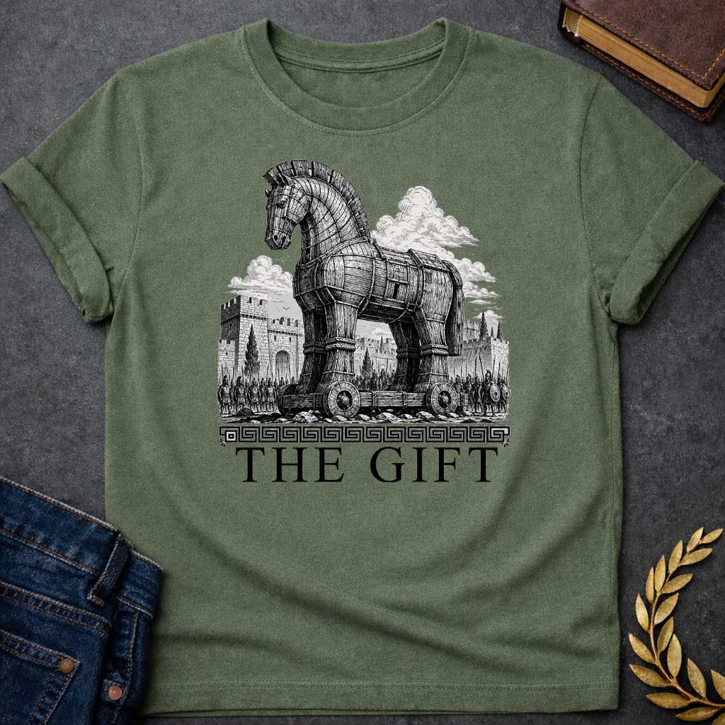 Military Green T-shirt with a graphic in black featuring an exceptionally detailed fine-line engraving-style illustration of the Trojan Horse towering over the walls of Troy, surrounded by crowds of armored Greek soldiers with spears and shields, set against dramatic billowing clouds. A Greek meander border separates the scene from large bold classical serif text below reading "The Gift" — an ironic reference to the Greek legend of the Trojan War