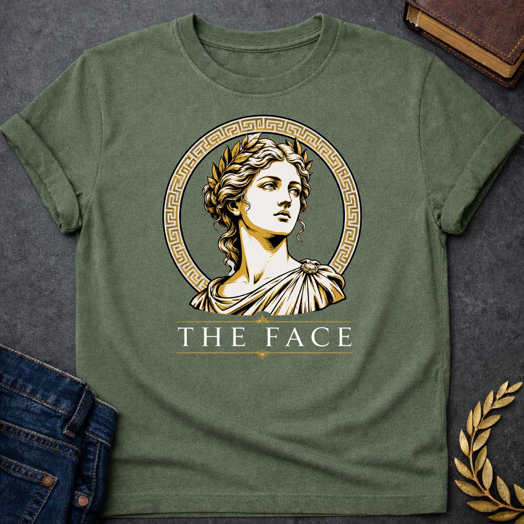 Military Green T-shirt with a classical Greek graphic featuring a gold and cream vector portrait of Helen of Troy in profile. She wears a golden laurel wreath and a traditional draped chiton, looking upward with a serene expression. The portrait is framed by a circular border with a gold Greek key (meander) pattern. Below the emblem, the text "THE FACE" is written in a clean, elegant white serif font between horizontal gold accent lines.