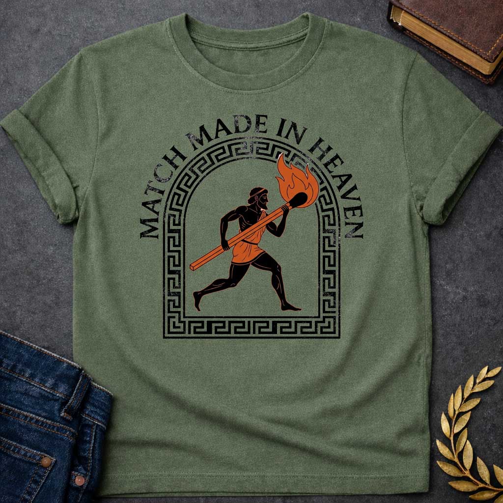 Military Green T-shirt with A graphic in an ancient Greek Black-Figure pottery style featuring Prometheus running while carrying a massive, burning match stick. He is depicted in black silhouette with terracotta-orange details on his tunic and the flame. The figure is framed by a black Greek key meander arch. Above the design, the pun "MATCH MADE IN HEAVEN" is written in an arched, bold black serif font.
