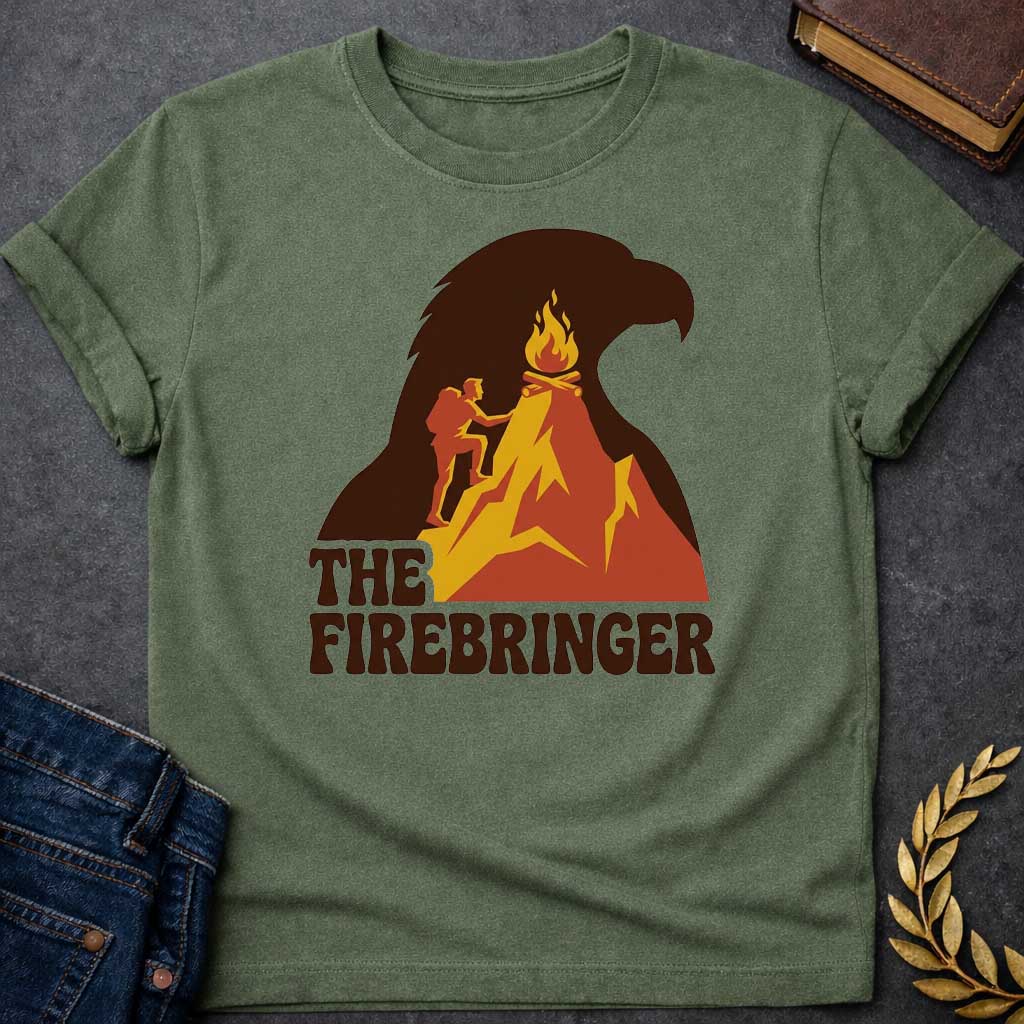 Military Green T-shirt with a retro, outdoor-style t-shirt graphic referencing Prometheus. It features a silhouette of a hiker with a backpack climbing an orange and yellow mountain peak toward a campfire at the top. The entire mountain scene is set against a large background silhouette of an eagle's head in dark brown. Below the image, the text "THE FIREBRINGER" is written in a bold, stylized 1970s-style brown font.