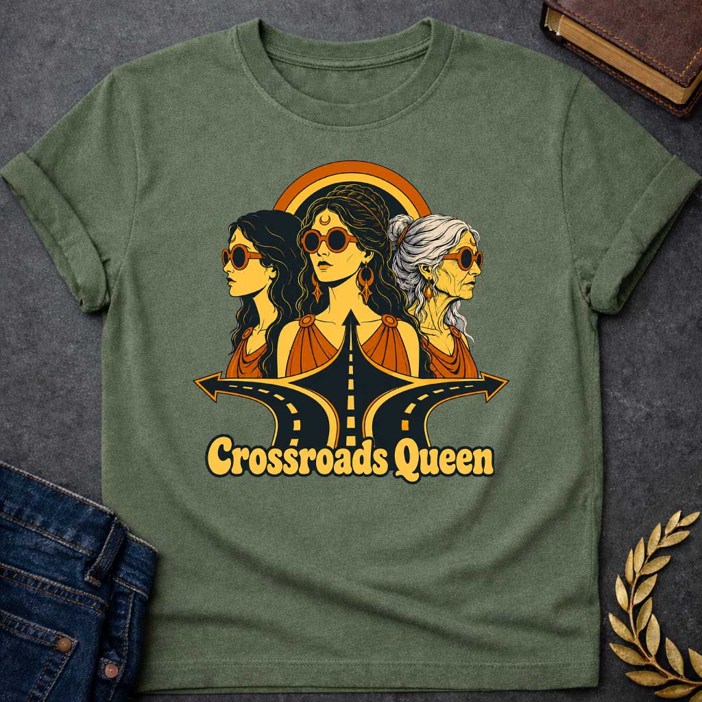 Military Green T-shirt with a Glamorous retro illustration of Hecate as 'Crossroads Queen' in gold and orange with 70s aesthetic. Three female faces wear oversized round sunglasses and gold jewelry including crescent moon symbols and hoops. Center figure wears a crescent moon bindi. All wear draped orange clothing. A golden halo radiates behind them. Below, stylized black roads with yellow center lines converge at a crossroads. Text reads 'Crossroads Queen' in gold.