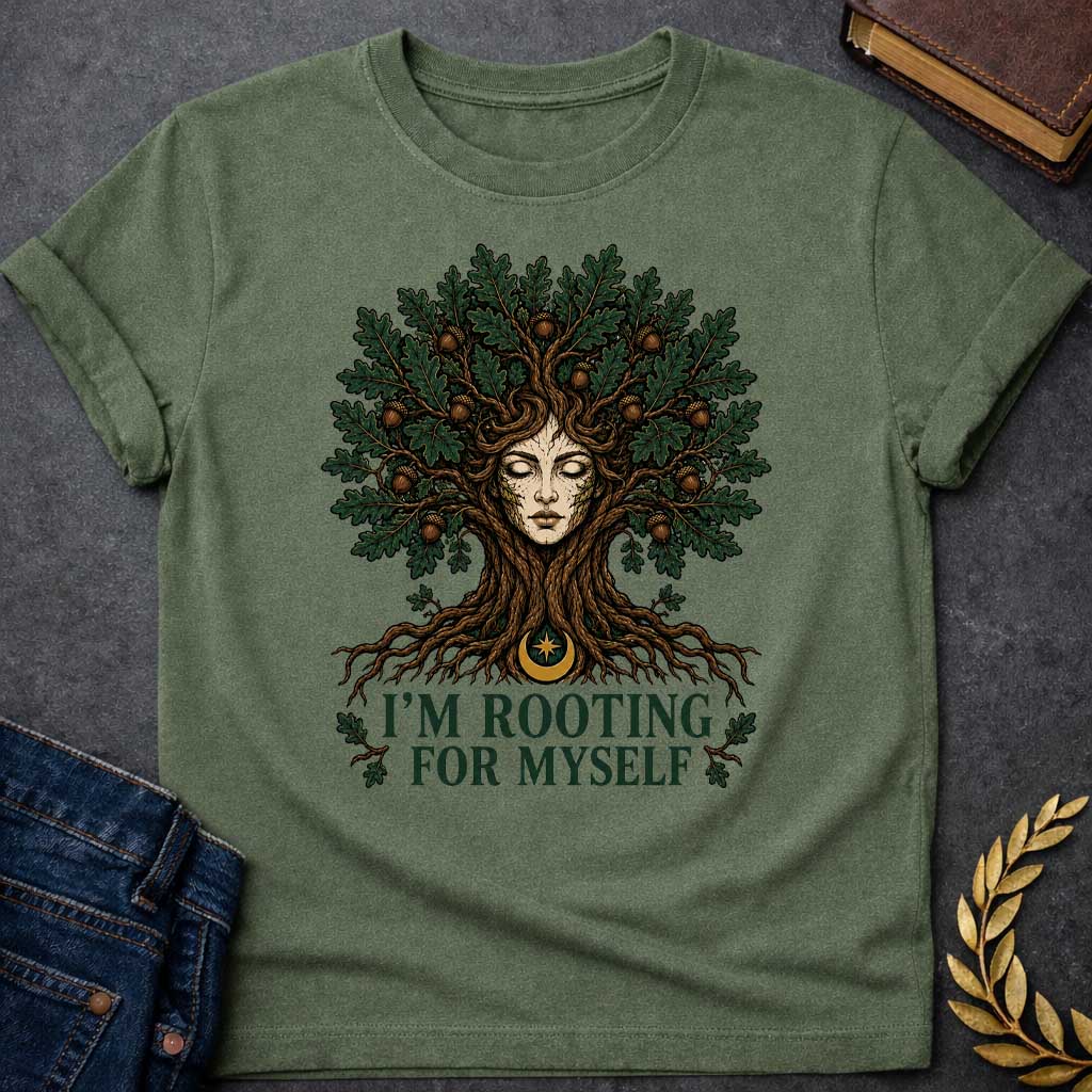 Military Green T-shirt with a cottagecore-style graphic featuring a detailed illustration of an oak tree dryad or nature spirit. Her serene, closed-eyed face forms the center of the tree trunk, with gnarled roots expanding below and a massive canopy of dark green oak leaves and brown acorns spreading above. Underneath the roots, a pun-based tagline reads "I'M ROOTING FOR MYSELF" in a bold, clean green serif font.