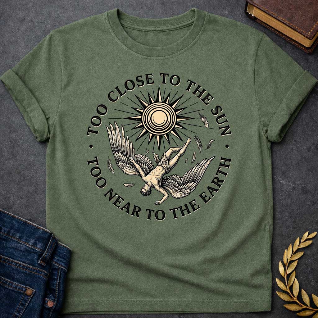 Military Green t-shirt with a vintage engraved-style illustration. A winged figure of Icarus plummets downward upside down as loose feathers drift through the air beneath a large, radiating sun emblem. Encircling the detailed central artwork, bold black serif text reads "TOO CLOSE TO THE SUN" along the top arch and "TOO NEAR TO THE EARTH" along the bottom curve.
