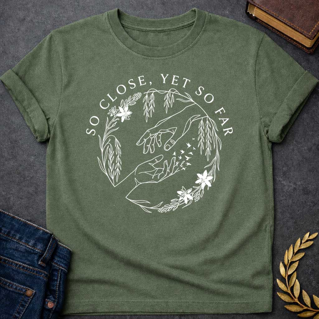 Military Green t-shirt in delicate fine-line style: two reaching hands almost touch, with one hand dissolving into a flock of small birds mid-fingertip, evoking Orpheus and Eurydice. Willow branches and small flowers form a circular wreath around the scene, with elegant serif text arcing above