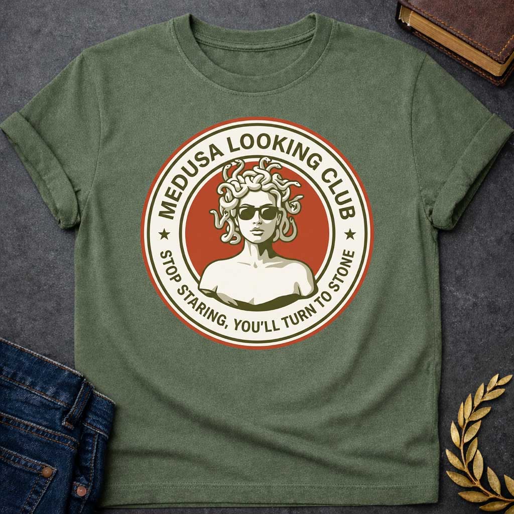 Military Green t-shirt in retro badge style: a cool, sunglasses-wearing Medusa with snake hair stands confidently against a burnt-orange circle. Cream and olive-green ring text reads "Medusa Looking Club" above and "Stop Staring, You'll Turn to Stone" below, with two stars flanking the design.