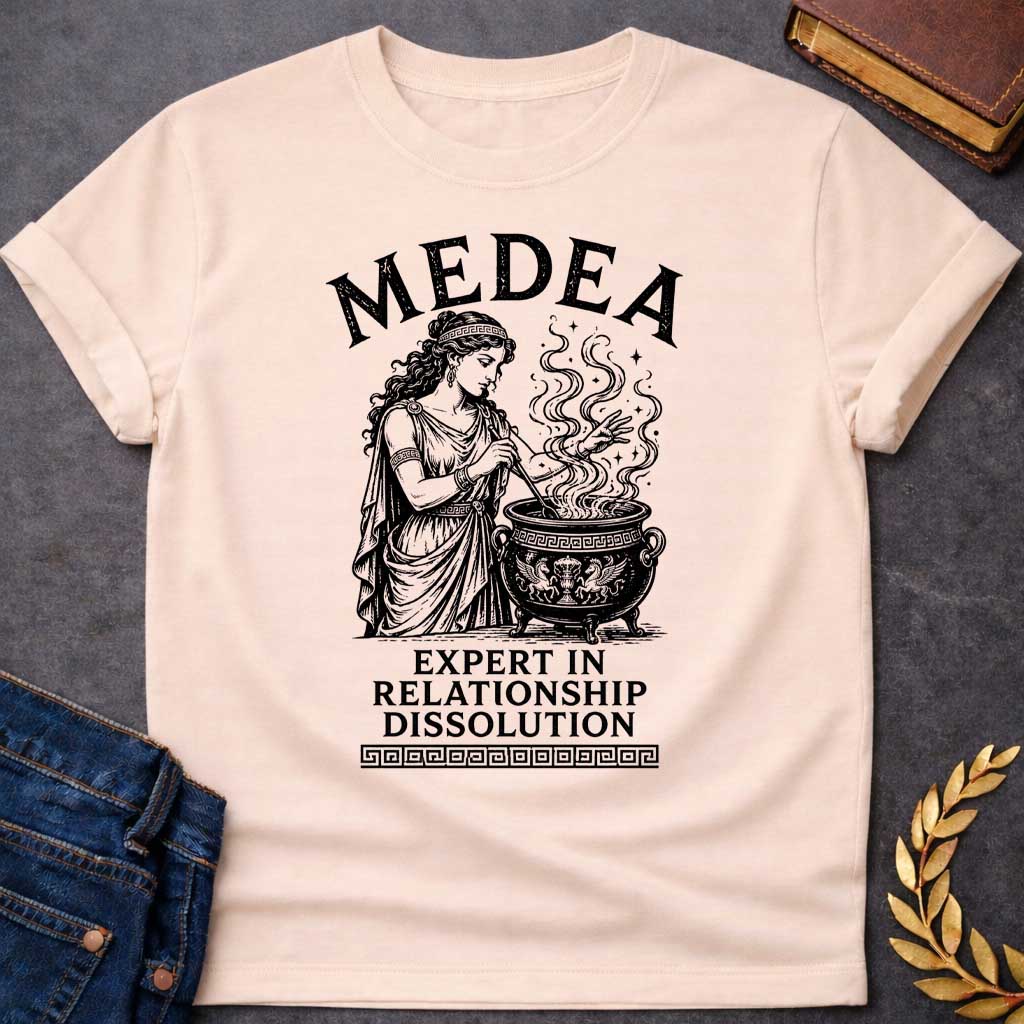 Natural T-shirt with a Classical engraving of Medea, the legendary Greek sorceress, in flowing draped robes with Greek key pattern headband. She stirs a decorative cauldron with magical swirling smoke and stars rising dramatically from within. Black and white line art style with intricate detailing. Text reads 'Medea' above and 'Expert in Relationship Dissolution' below with Greek key border. Dark humor celebrates Medea's infamous reputation for magical vengeance and relationship destruction.