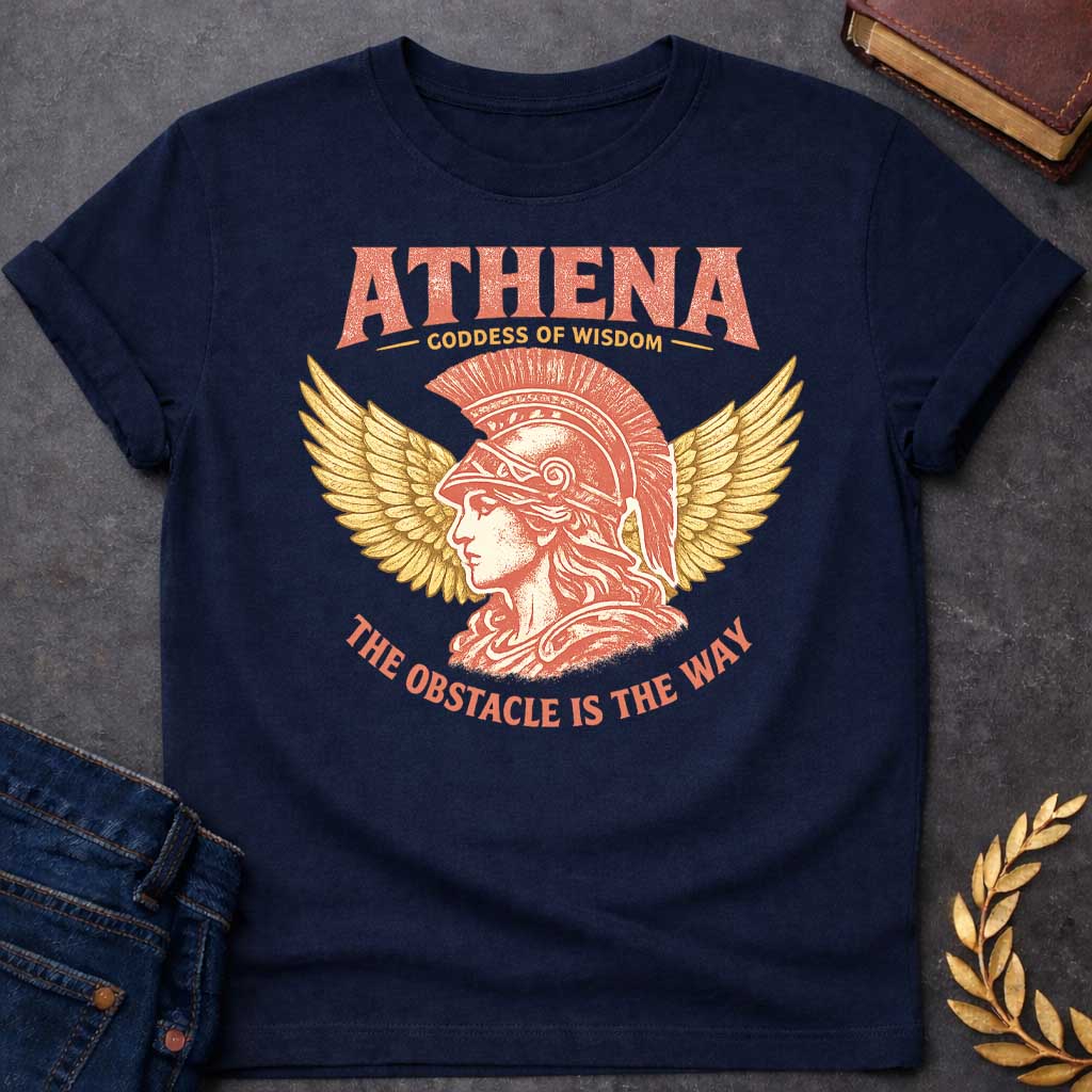 Navy t-shirt graphic featuring a side-profile illustration of Athena wearing a Corinthian helmet with a red plume, flanked by large golden wings. Text reads "ATHENA – Goddess of Wisdom" arched above and "The Obstacle Is the Way" curved below, in a vintage Greek mythology style with rose and gold tones