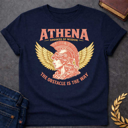 Navy t-shirt graphic featuring a side-profile illustration of Athena wearing a Corinthian helmet with a red plume, flanked by large golden wings. Text reads "ATHENA – Goddess of Wisdom" arched above and "The Obstacle Is the Way" curved below, in a vintage Greek mythology style with rose and gold tones