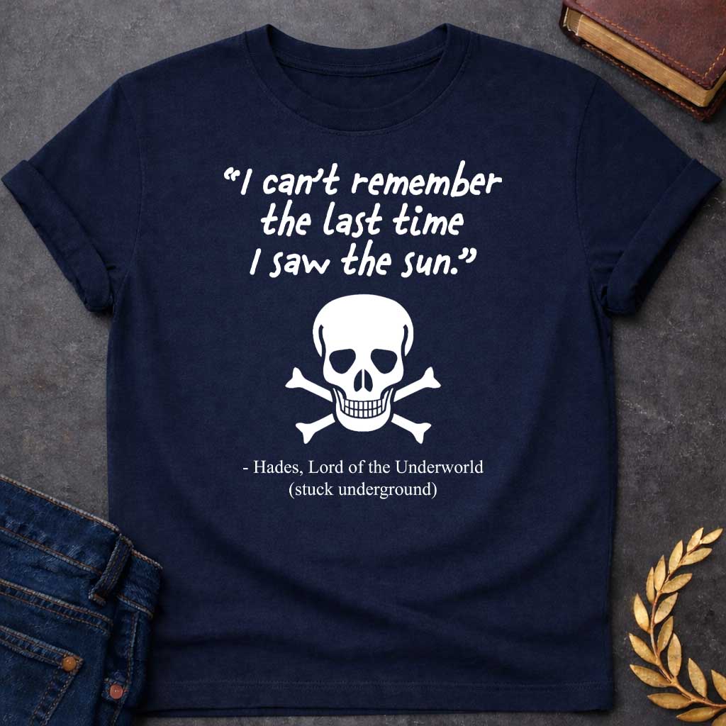 Navy T-shirt graphic in black and white featuring a handwritten-style quote reading "I can't remember the last time I saw the sun." above a classic skull and crossbones illustration, with the humorous attribution below reading "- Hades, Lord of the Underworld (stuck underground)