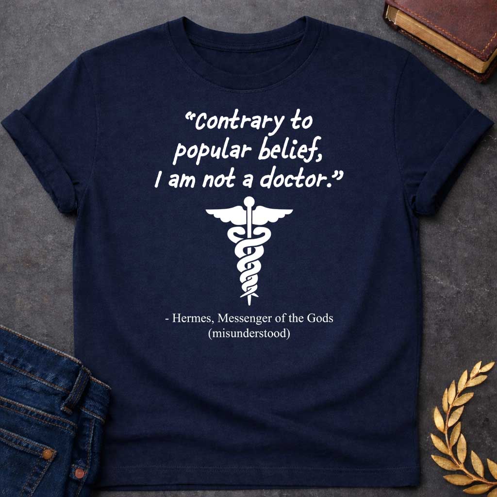 Navy T-shirt graphic in white text featuring a handwritten-style quote reading "Contrary to popular belief, I am not a doctor." above a white caduceus symbol, with the humorous attribution below in serif text reading "- Hermes, Messenger of the Gods (misunderstood)," playing on the common confusion between Hermes' caduceus and the medical symbol