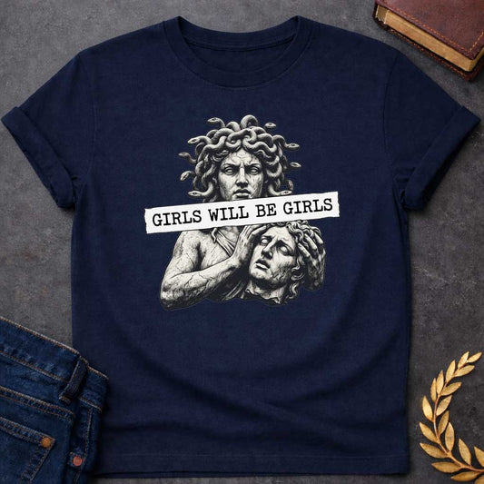 Navy T-shirt graphic in black and white featuring a detailed stone sculpture-style illustration of Medusa with snake hair looming above a distressed male figure clutching his head in anguish, with a torn paper banner across the middle reading "Girls Will Be Girls" in bold typewriter font — a humorous feminist nod to the Greek mythology story of Medusa