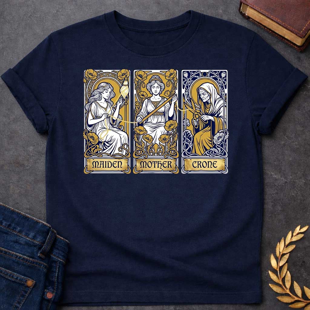 Navy T-shirt graphic featuring three Art Nouveau-style tarot card panels in navy, gold, and white, each depicting one of the Moirai, the Greek Fates, as the triple goddess archetypes. The first panel shows the Maiden as a young woman spinning a golden thread from a spindle amid poppies, labelled "Maiden." The middle panel shows the Mother as a composed woman measuring the thread with a ruler surrounded by blooming poppies, labelled "Mother." The third panel shows the Crone as an elderly hooded woman holding