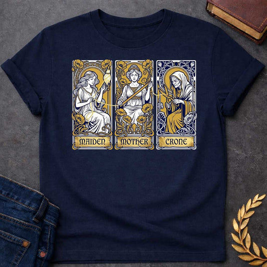 Navy T-shirt graphic featuring three Art Nouveau-style tarot card panels in navy, gold, and white, each depicting one of the Moirai, the Greek Fates, as the triple goddess archetypes. The first panel shows the Maiden as a young woman spinning a golden thread from a spindle amid poppies, labelled "Maiden." The middle panel shows the Mother as a composed woman measuring the thread with a ruler surrounded by blooming poppies, labelled "Mother." The third panel shows the Crone as an elderly hooded woman holding