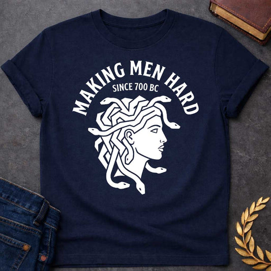 Navy T-shirt graphic white featuring a bold flat graphic side-profile illustration of Medusa with snake hair, in a minimalist ancient Greek coin or seal style. Bold arched text above reads "Making Men Hard" with smaller text below it reading "Since 700 BC" — a witty double entendre referencing Medusa's mythological power to turn men to stone