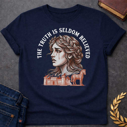 Navy T-shirt with a A Greek mythology design featuring a detailed woodblock-engraving style illustration of a crying Cassandra in profile. She wears a laurel wreath, with tears streaming down her face. Arched above her is the text "THE TRUTH IS SELDOM BELIEVED" in a bold white serif font. Below her portrait, a burning ancient city wall and the Trojan Horse are illustrated in a fine-line, terracotta-orange style.