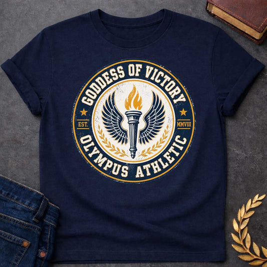 Navy T-shirt with an Official athletic seal in navy blue, cream, and gold featuring a torch with large outstretched wings symbolizing Nike, the goddess of victory. Flames burn from the torch. Olive wreaths frame either side. Text reads 'GODDESS OF VICTORY' and 'OLYMPUS ATHLETIC' around the circular border with 'EST. MMVIII.' Distressed vintage texture and gold stars enhance the emblem. Celebrates athletic achievement and triumph.
