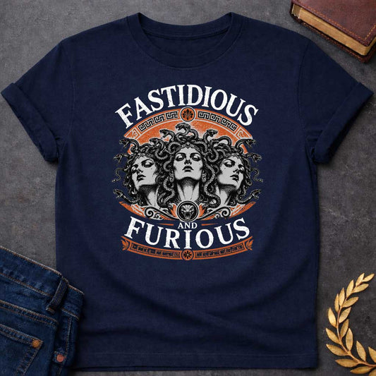 Navy T-shirt with a Humorous design combining 'Fast and Furious' with Greek mythology. Text reads 'FASTIDIOUS AND FURIOUS' in distressed lettering surrounding three faces of Medusa in black and white engraving style. Detailed serpents with individual scales form her hair. Greek key pattern borders in orange frame the composition with decorative sun motifs and a small snake head icon at center. Blends classical mythology with contemporary pop culture humor and clever wordplay.