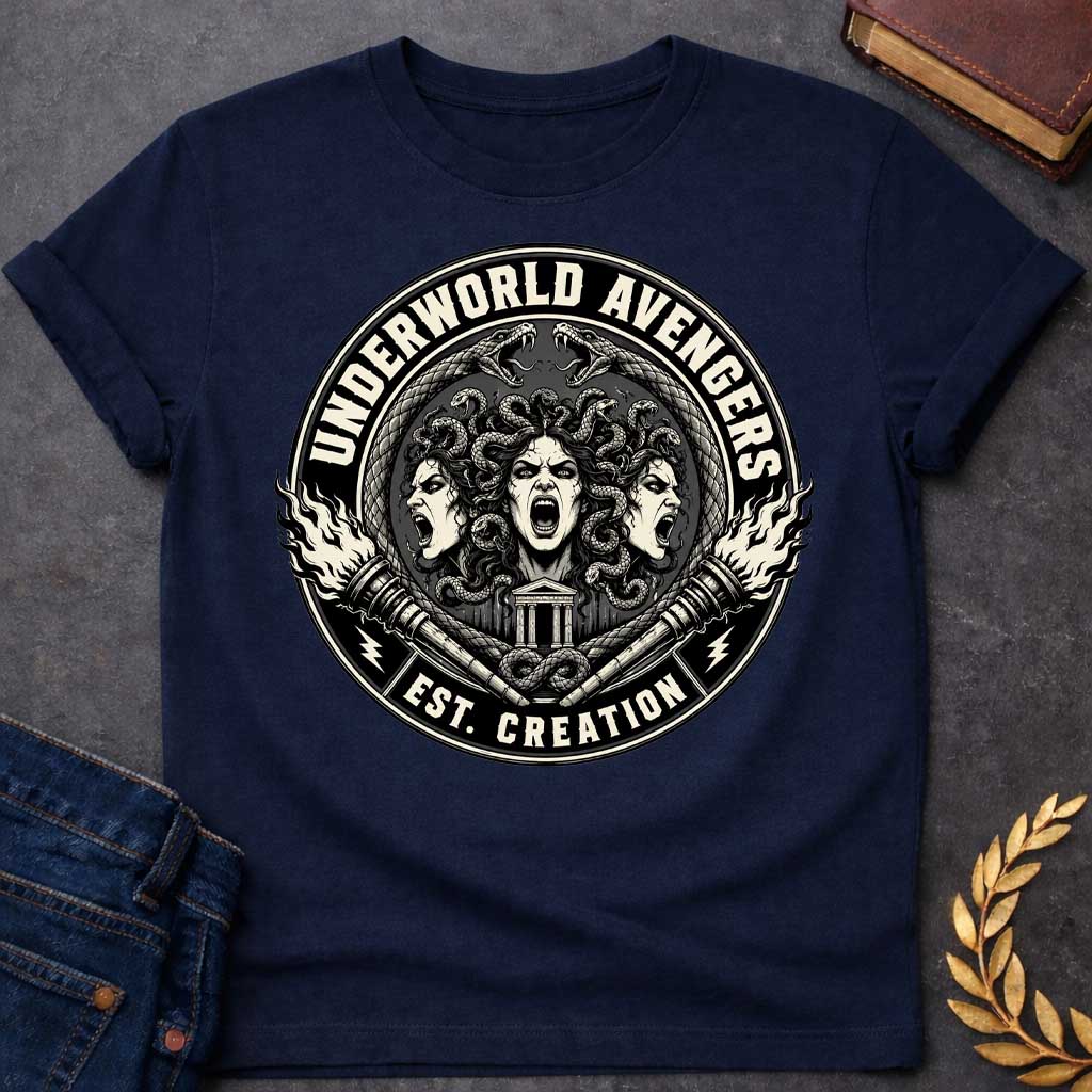 Navy T-shirt with an Official emblem design for the 'Underworld Avengers,' a parody combining Greek mythology with Marvel. Three Fury faces with detailed serpent hair display aggressive expressions. A Greek temple sits below, framed by crossed ornate daggers. Flames and lightning bolts accent the circular seal in vintage badge style. Text reads 'Underworld Avengers: Est. Creation.' Black and cream colors celebrate a team of divine vengeance and supernatural justice.