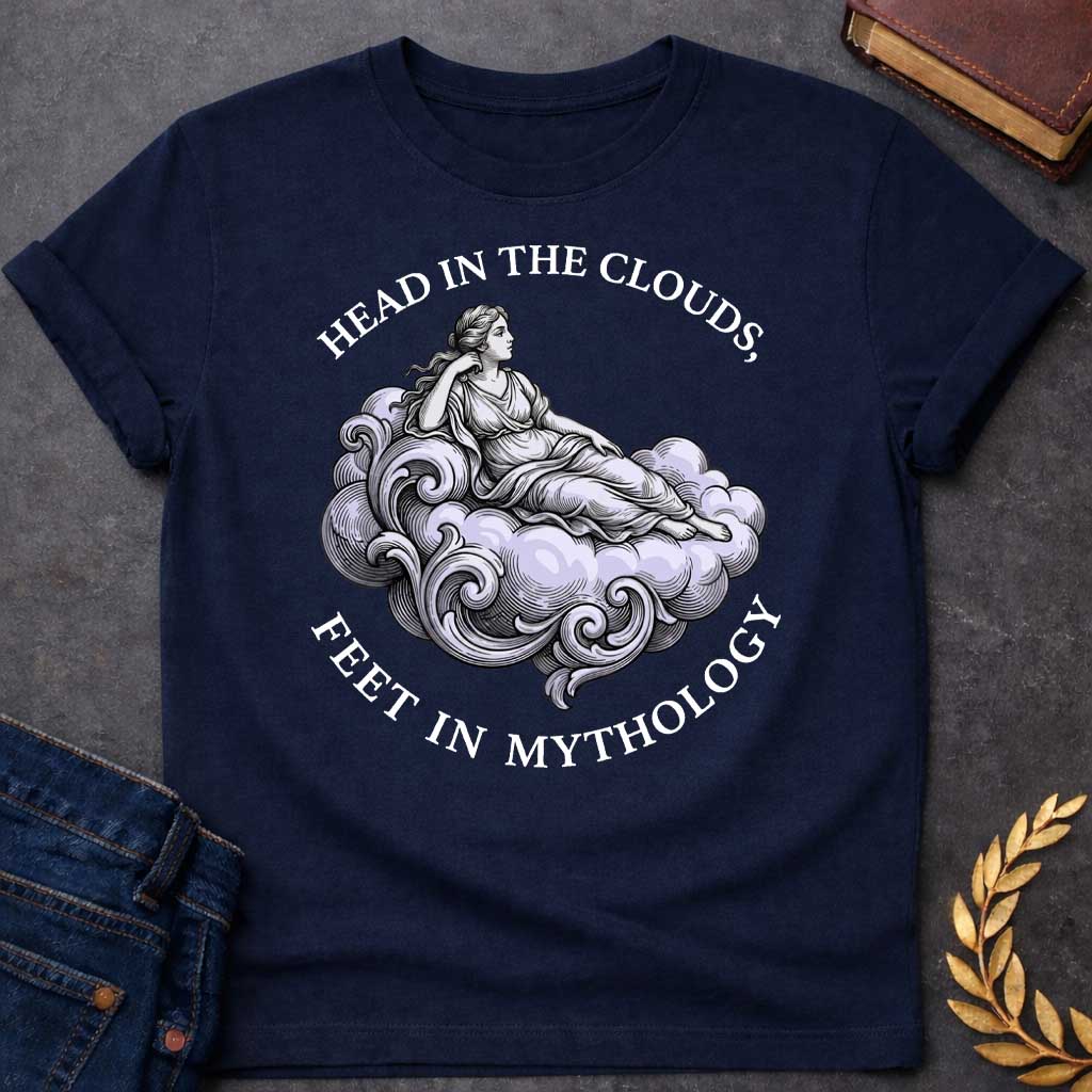 Navy T-shirt with a classical Greek mythology t-shirt design featuring a detailed engraving-style illustration. A woman in a traditional draped chiton relaxes gracefully, reclining on a large, swirling baroque-style cloud shaded in a pale purple hue. Arched above her is the text "HEAD IN THE CLOUDS," and curved inversely below the cloud is "FEET IN MYTHOLOGY," all written in a clean white serif font.