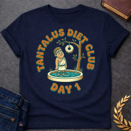 Navy t-shirt with A cartoon illustration, Standing in a small shallow pool next to a tree, a sad Greek man in a toga gazes glumly at a frosted donut with sprinkles dangling just out of reach from a branch. Chunky, retro orange and teal text arches over the graphic reading "TANTALUS DIET CLUB", with "DAY 1" featured prominently at the bottom.