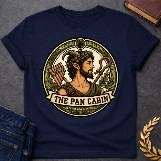 Navy t-shirt with a Pan Greek mythology cabin design featuring the god of the wild and shepherds with curved goat horns, pointed ears, leafy crown, and rustic robes. Surrounded by panpipes, a shepherd’s crook, oak leaves, acorns, and Greek key details in an earthy green and gold circular emblem. Text reads “The Pan Cabin” and “God of the Wild & Shepherds,”